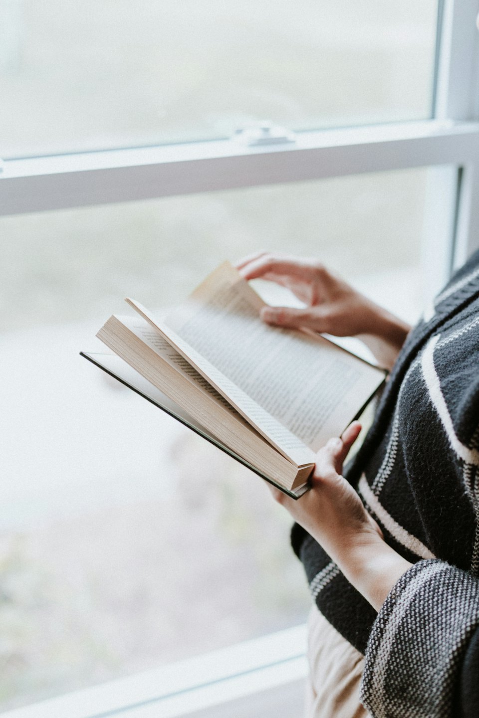 Person wearing a patterned top turns a page of their book.