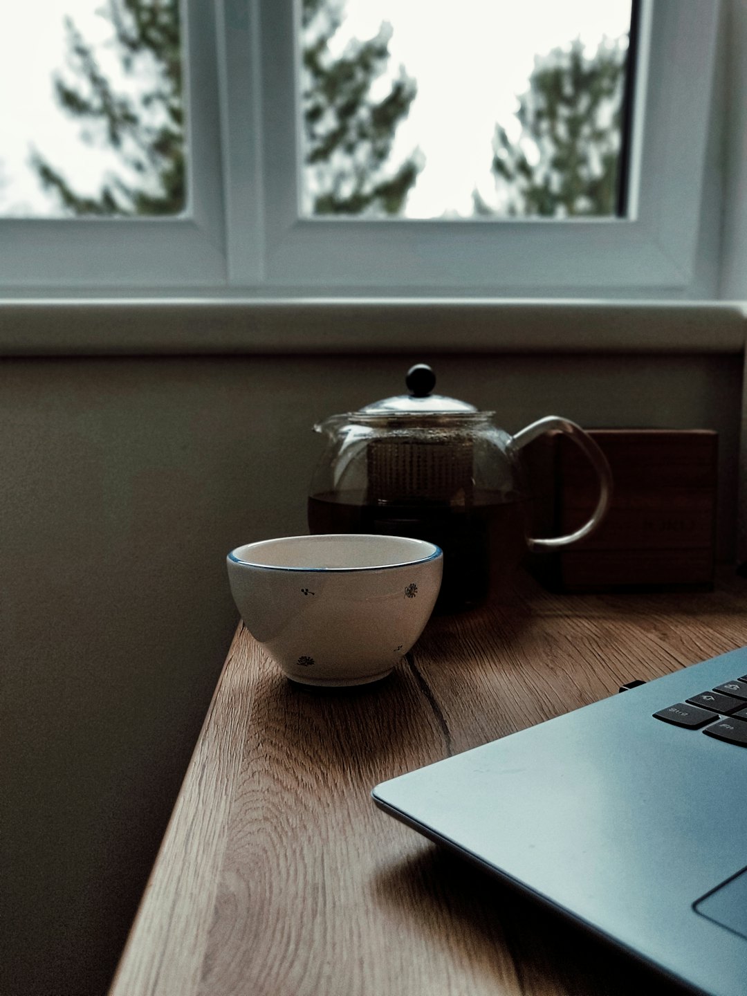 A workspace with a teapot and laptop on a wooden desk.